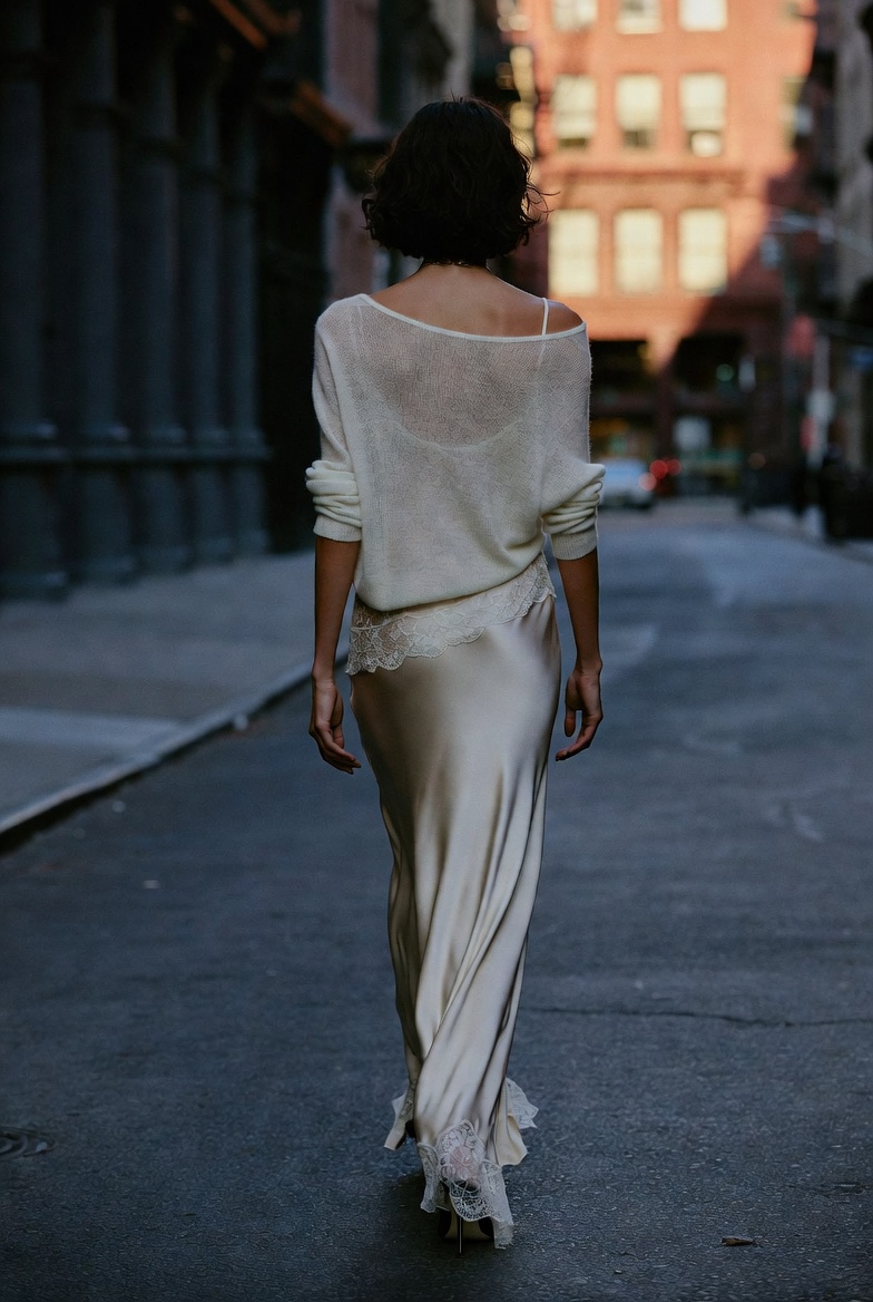 A woman in a lace silk slip dress layered under a fine cashmere knit with heels in SoHo at dusk